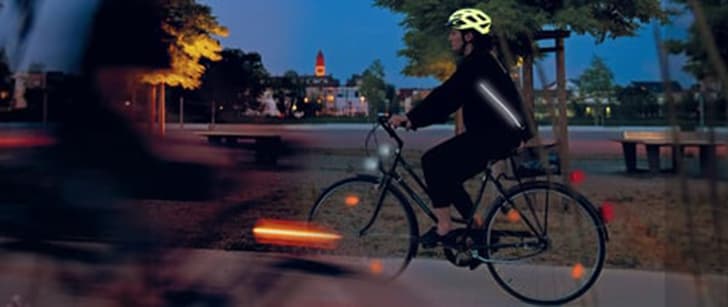 Cycliste portant une veste munie de réflecteurs et un casque réfléchissant, pédalant en pleine nuit sur une voie cyclable.