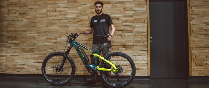 Bike World Verkäufer präsentiert ein Elektro Mountainbike vor einer Holzwand