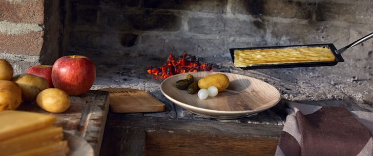 Raclettepfanne und ein Teller mit Kartoffeln und Silberzwiebeln