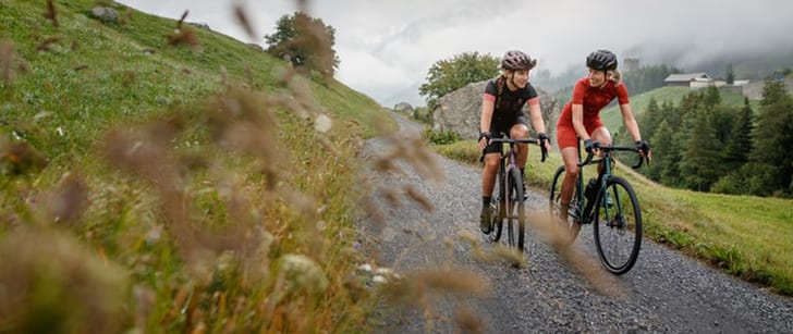 Due amiche con casco da ciclismo pedalano con le loro gravel bike su un sentiero di ghiaia