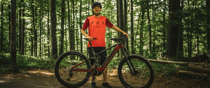 Ivan, membro della community Bike World, sorride in posa dietro alla sua mountain bike elettrica nel bosco.