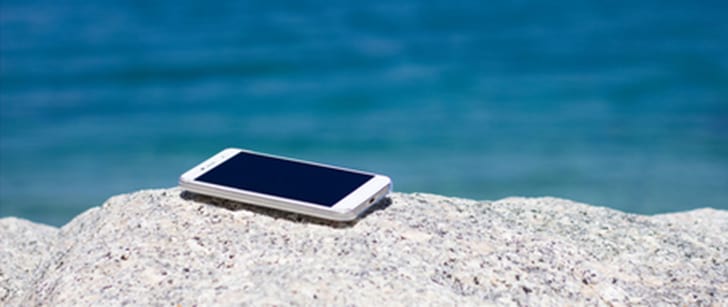 Un smartphone sur une pierre grise, avec la mer en toile de fond.