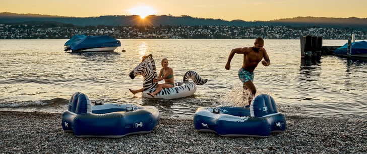 Un uomo e una donna si godono l&apos;estate ammirando il tramonto sul lago. L&apos;uomo corre fuori dall&apos;acqua e la donna è seduta su una zebra gonfiabile.