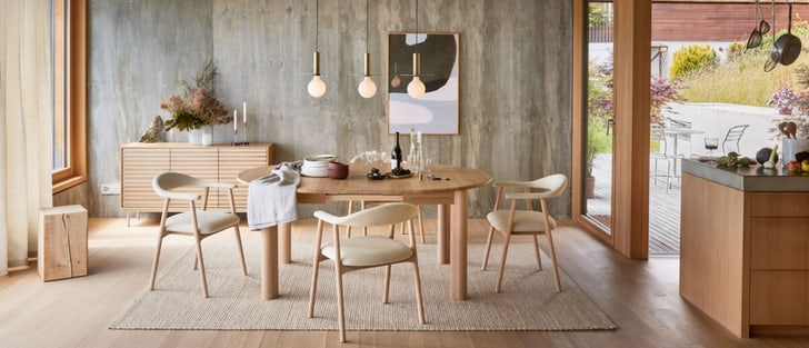 Modern gestaltetes Esszimmer mit runder Holztisch, skandinavischen Stühlen und minimalistischen Pendelleuchten, neben einer Betonwand und Blick auf eine Terrasse