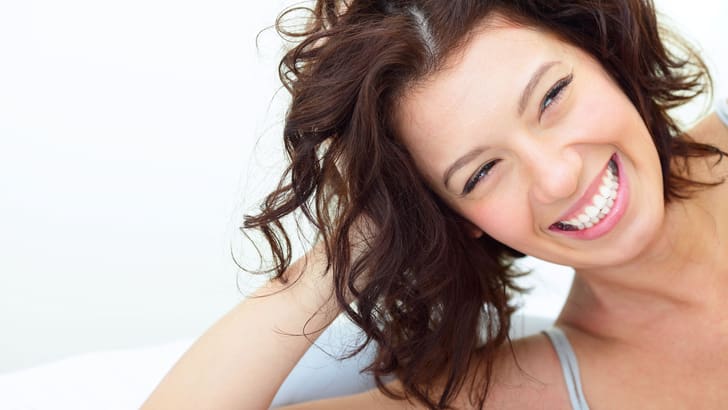 Une femme appuyée sur une main affiche un large sourire et montre ses dents blanches.