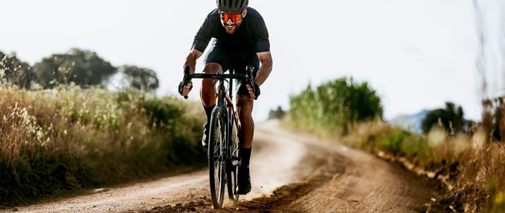 Cycliste avec le sourire au lèvres roulant sur un chemin de terre au guidon de son vélo Gravel.