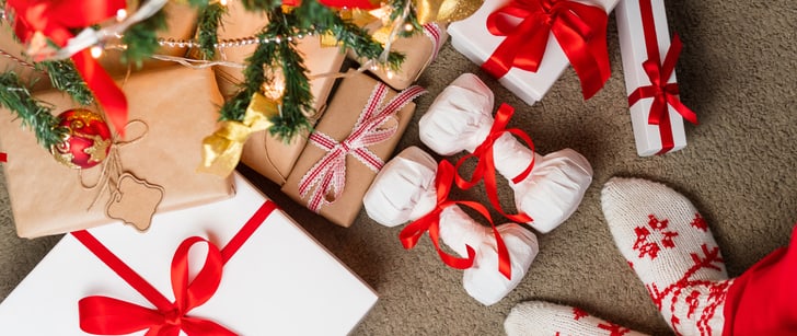 Zwischen Geschenken unter einem Weihnachtsbaum liegen zwei Geschenke in Form von zwei kleinen Hanteln.