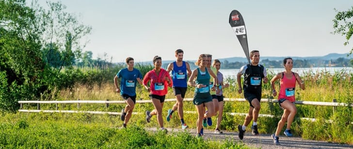 Un groupe mixte portant des dossards court sur un sentier non goudronné, un lac à l’arrière-plan.