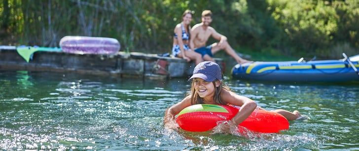 En été, une fillette se baigne dans un lac avec une bouée gonflable, ses parents la regardant depuis le ponton.