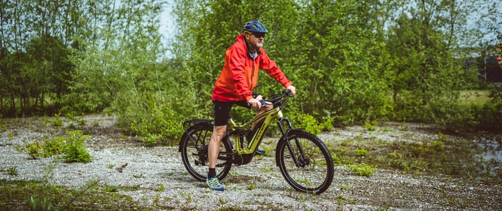 En tenue de sport outdoor, Urs, collaborateur de Bike World, en selle sur son vélo de trekking électrique vert.