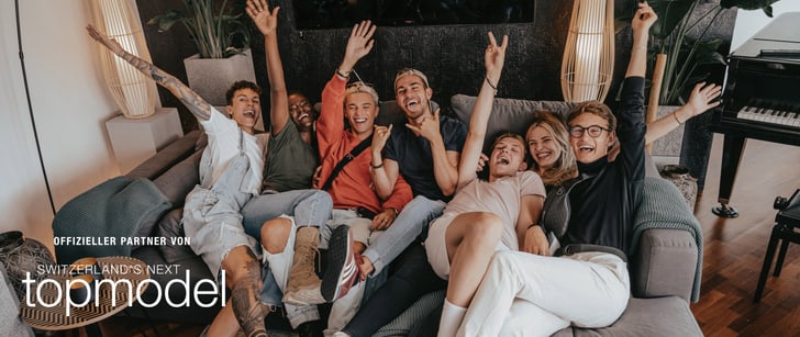 Sieben attraktive junge Menschen liegen lachend auf einem Polstersofa