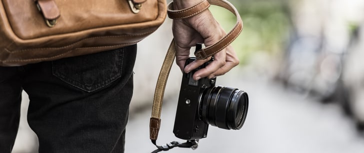 Un homme portant une sacoche en cuir tient un appareil photo numérique dans sa main droite.