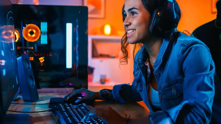 Une jeune femme joue sur ordinateur, des écouteurs sur la tête.