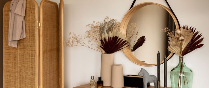 Trockenblumen in einer Vase auf einer Holzkomode mit einem runden Spiegel an der Wand