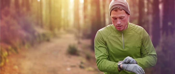 Un jeune homme fait son jogging dans la forêt en regardant sa montre au poignet