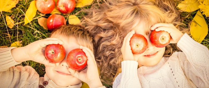 Una ragazza e un ragazzo sono stesi su un prato e tengono delle mele davanti agli occhi