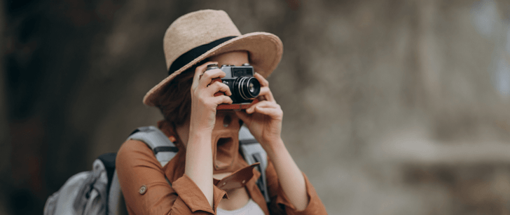 Una donna con un cappello di paglia e uno zaino fa foto con una fotocamera.