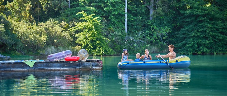 Eine vierköpfige Familie geniesst ihre Ferien in der Schweiz indem sie in einem Schlauchboot auf dem See herum rudern.