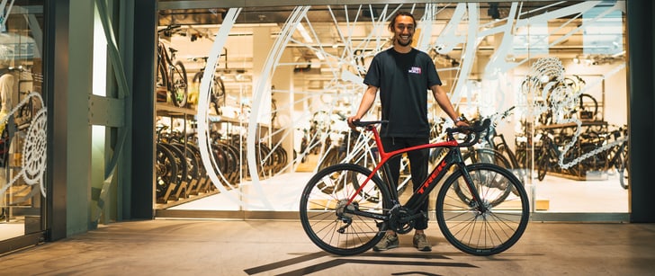 Un vendeur Bike World tout sourire présente un vélo de course devant le point de vente.