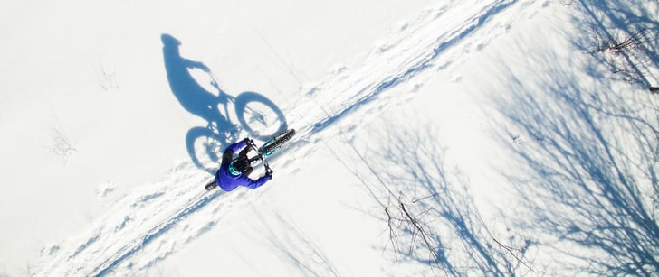 Vista dall&apos;alto di un ciclista di mountain bike con abiti invernali che pedala su un percorso innevato
