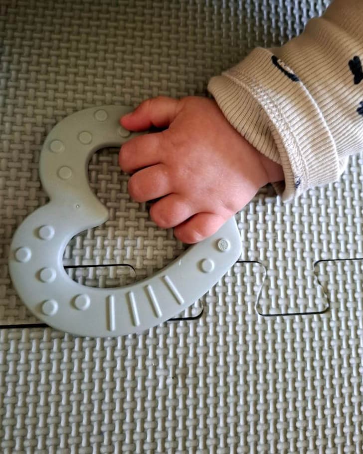 Une main d&apos;enfant tient un anneau de dentition en forme de cœur sur un tapis de jeu.