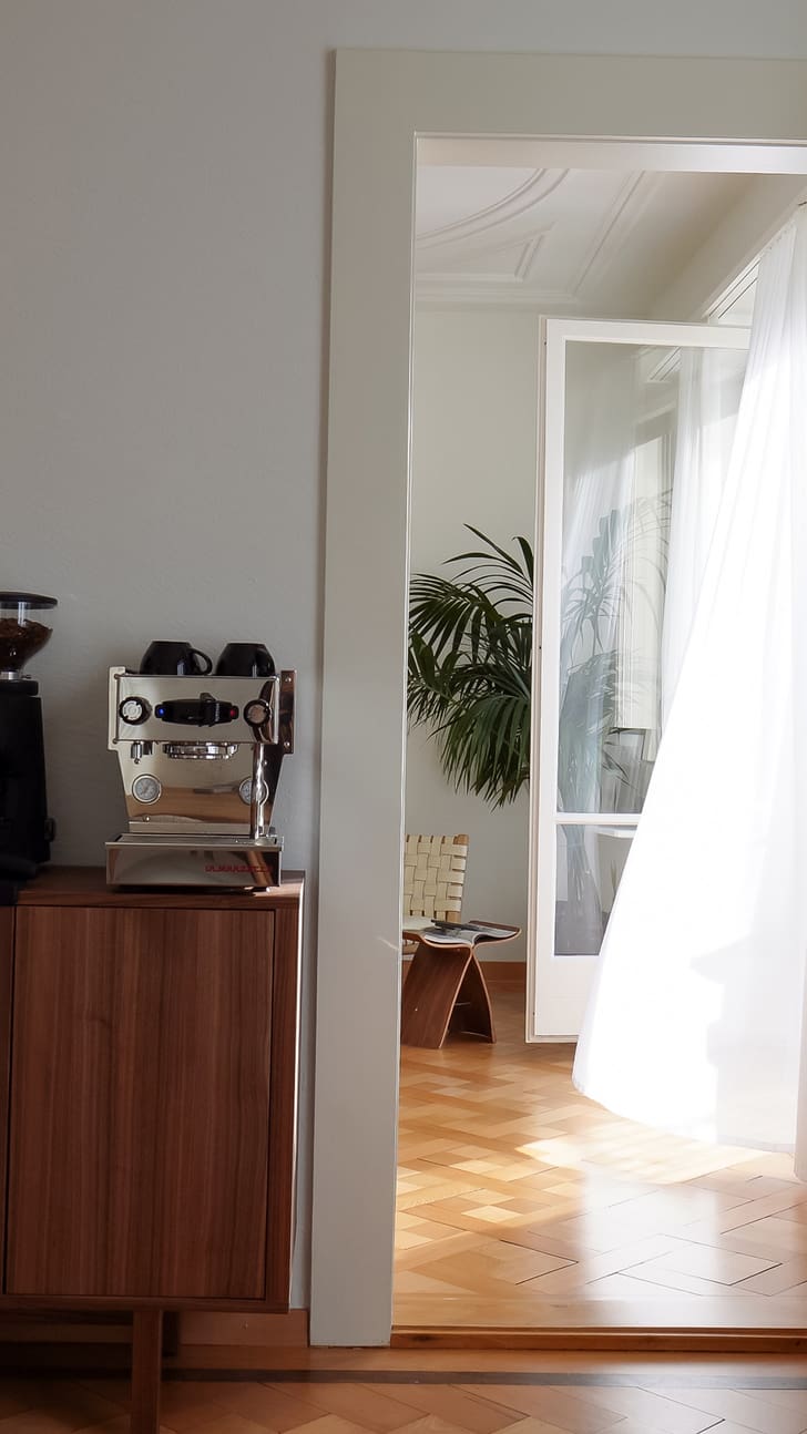 Vue sur une machine à café sur un meuble en bois à côté d&apos;un salon lumineux avec des plantes.