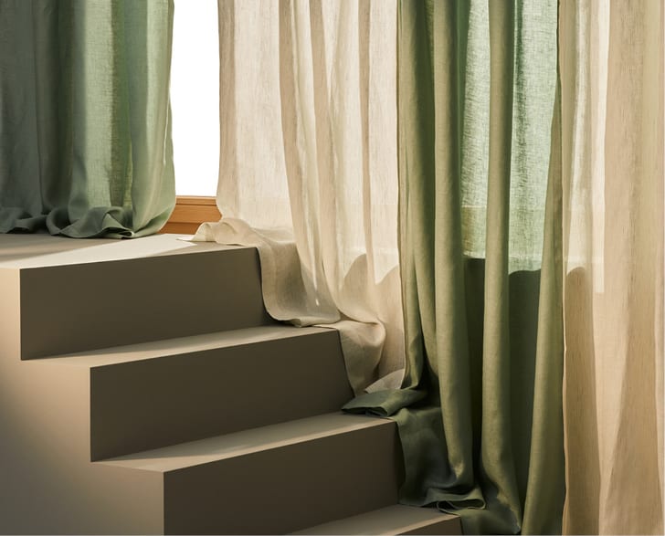Halbdurchsichtige Vorhänge in Grün und Beige, die über eine Treppe hängen.