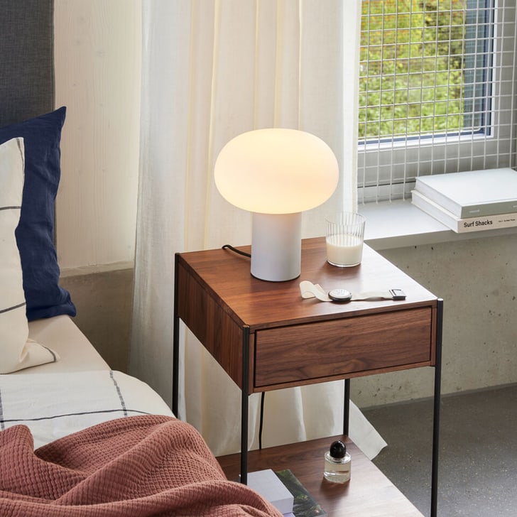 Table de nuit avec lampe, montre et verre a cote d&apos;un lit avec linge de lit bleu et rose.
