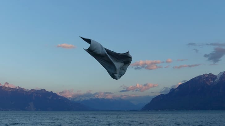 Ein Tuch schwebt über einem See mit Bergen im Hintergrund.