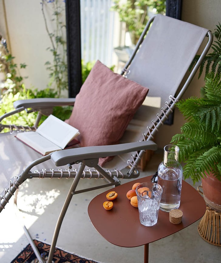 Liegestuhl mit Kissen und offenem Buch, daneben ein Tisch mit Aprikosen, Wasserflasche und Glas.