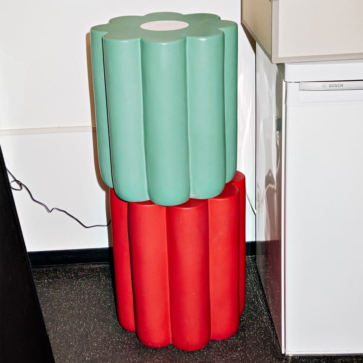 Deux tabourets cylindriques empilés en vert et rouge à côté d'un réfrigérateur.