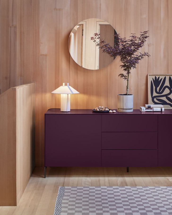 Sideboard in der Farbe Aubergine/Bordeaux-Rot mit Spiegel und Pflanze, umgeben von sanften Rottönen.  