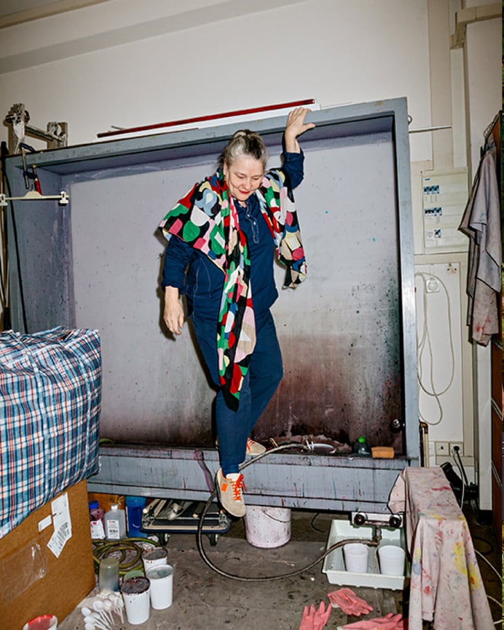 Sonnhild Kestler dans un atelier créatif, entourée de couleurs et de matériaux, portant une écharpe colorée.