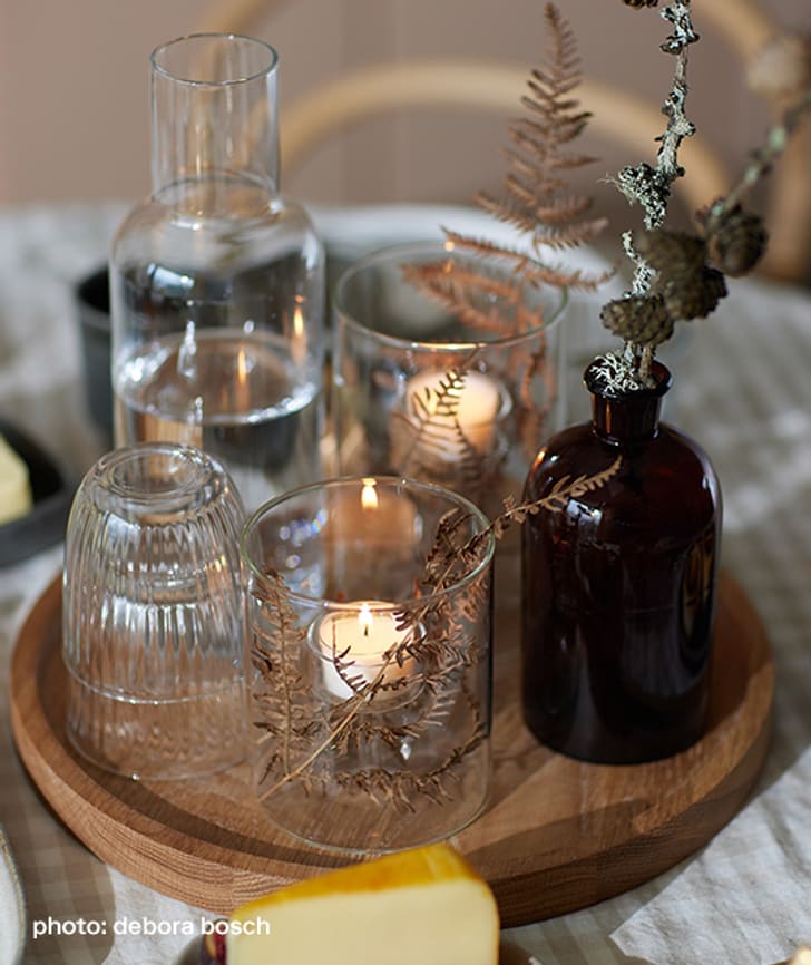 Bougies et fleurs séchées dans des verres sur un plateau.