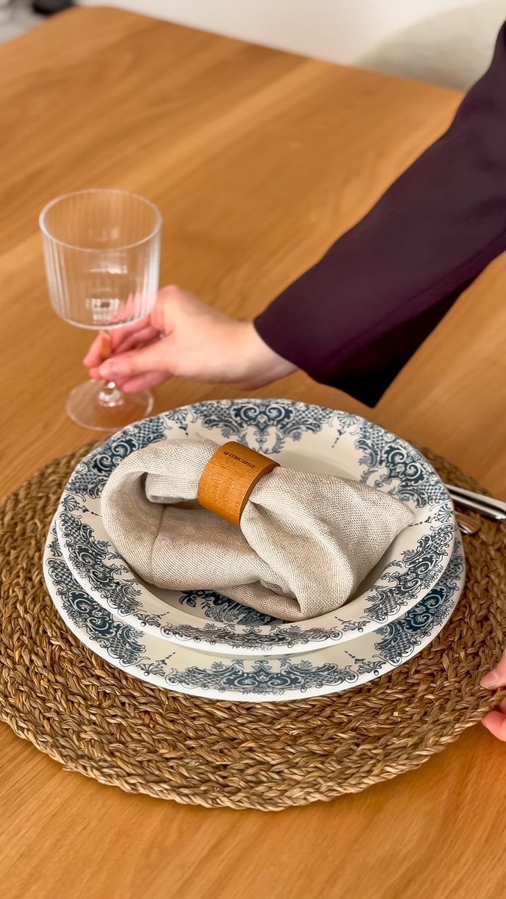 Une table dressée avec une assiette sur laquelle repose une serviette en tissu, et une main tenant un verre à vin.