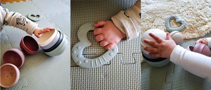 Babyhaende spielen mit stapelbaren Bechern und einem Beissring auf einer Spielmatte.