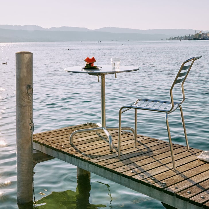 ﻿Sedia e tavolo in metallo zincato a caldo di Schaffner si trovano su un pontile di legno in riva al lago al tramonto.