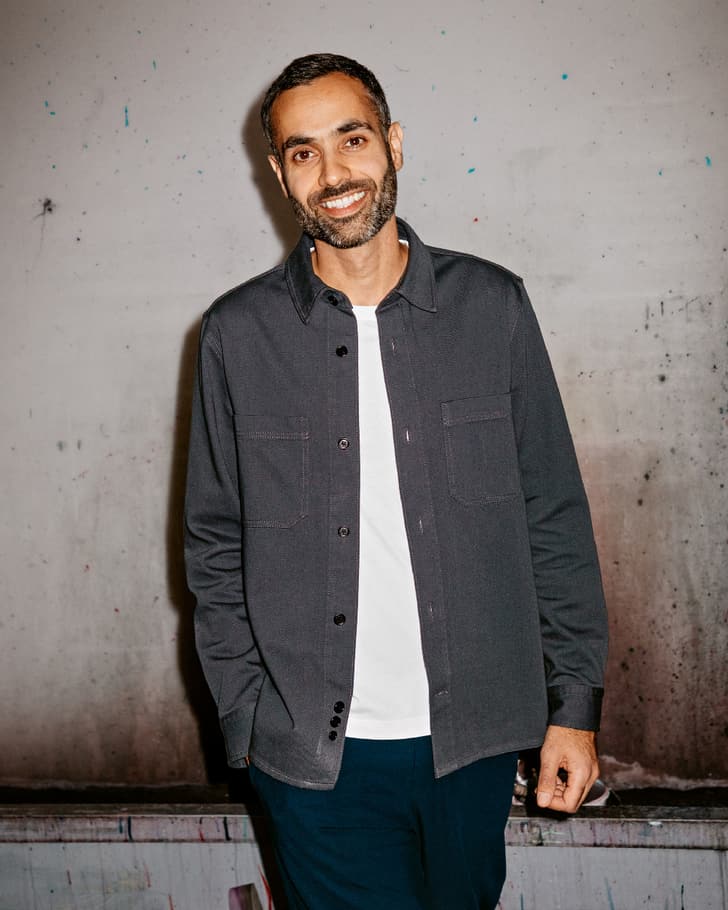 Personne portant un t-shirt blanc et une chemise gris foncé devant un mur.