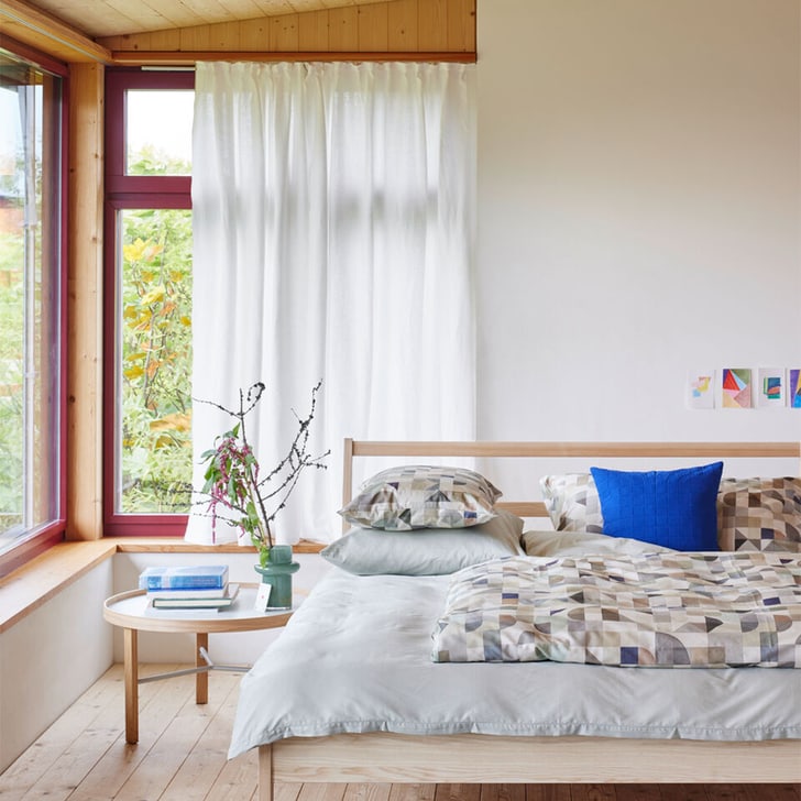 Chambre lumineuse avec lit en bois, linge de lit geometrique et coussin bleu.