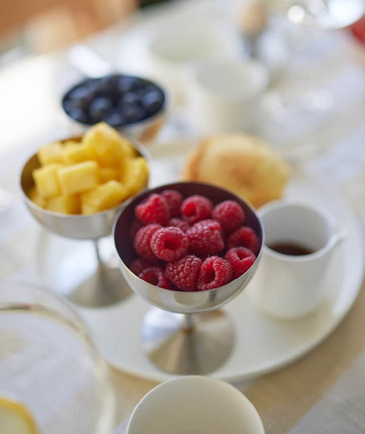 Frische Himbeeren, Ananas und Heidelbeeren in silbernen Schalen auf einem Frühstückstisch.
