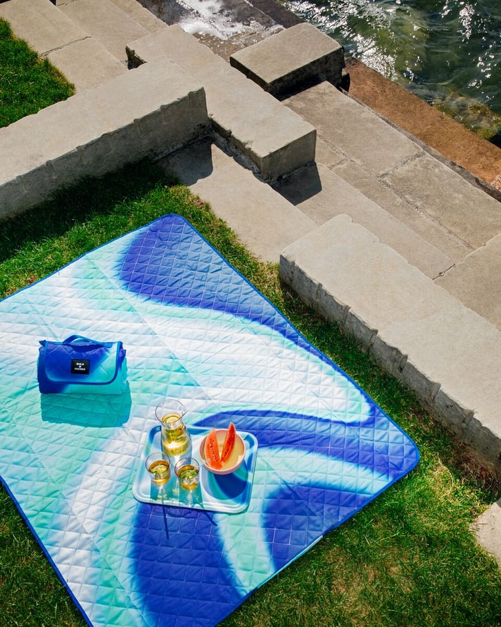 Coperta da picnic vicino all'acqua con bevande e anguria su un vassoio.