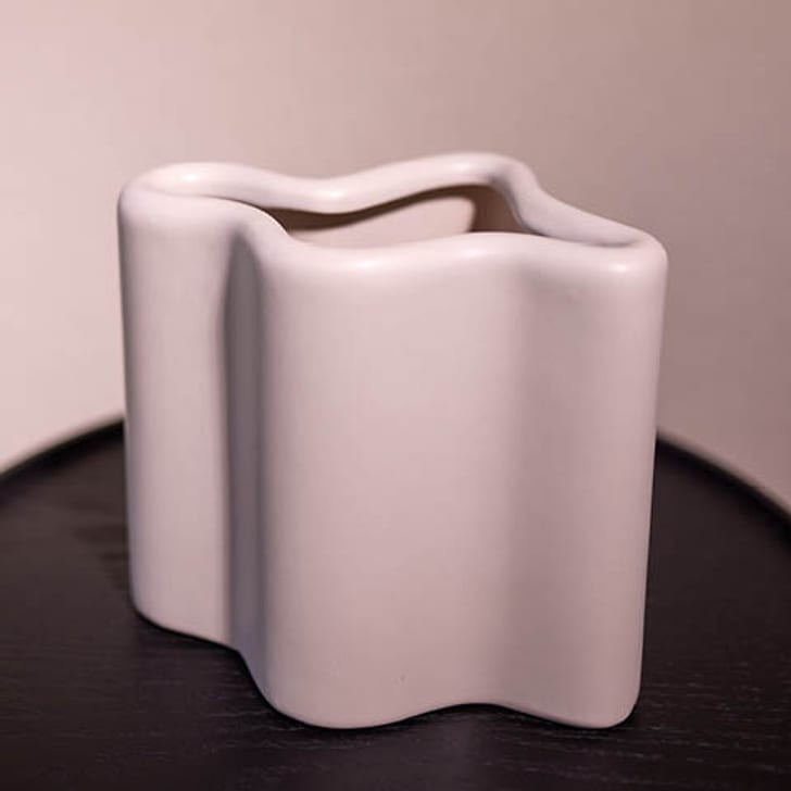 Weisse, wellenförmige Vase NOLA auf einem schwarzen Tisch.
