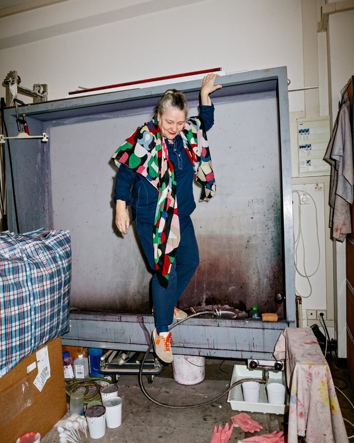 Sonnhild Kestler dans un atelier créatif, entourée de couleurs et de matériaux, portant une écharpe colorée.