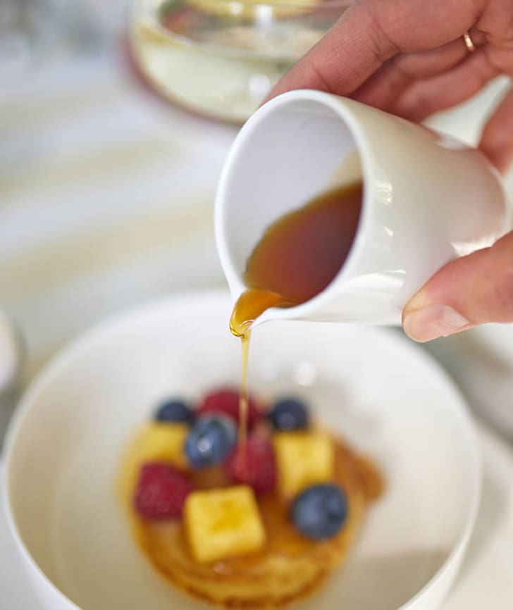 Sirup wird über Pancakes mit Früchten gegossen.