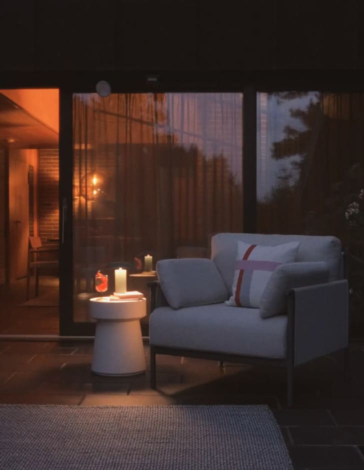 Fauteuil confortable sur une terrasse éclairée par des bougies, avec vue sur un intérieur chaleureusement illuminé.