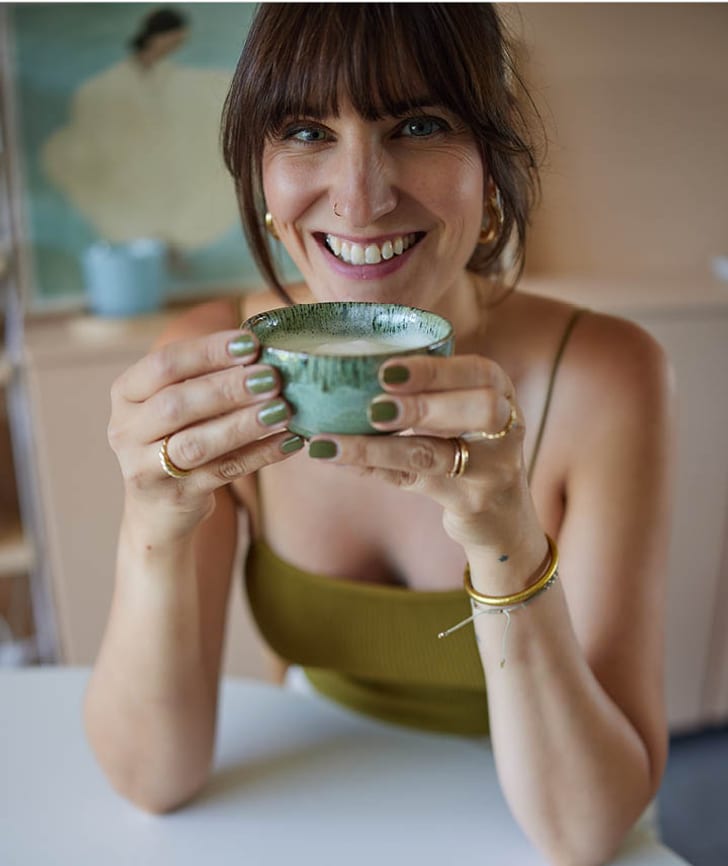 Frau haelt eine gruene Tasse mit beiden Haenden, ihre Naegel sind passend lackiert.