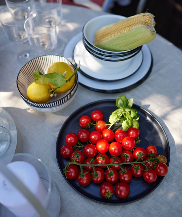 Tavolo con piatto di pomodori, basilico, limoni e pannocchie di mais.