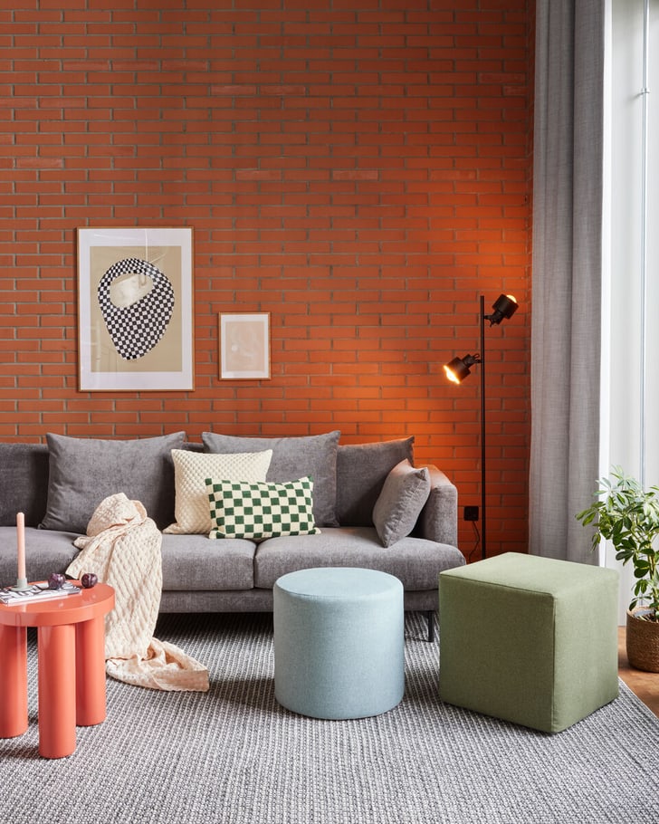 Modernes Wohnzimmer mit grauem Sofa, bunten Kissen und Ziegelwand.