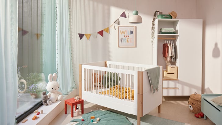 Helles in fröhlichen Farben eingerichtetes Babyzimmer mit einem Babybett in der Mitte