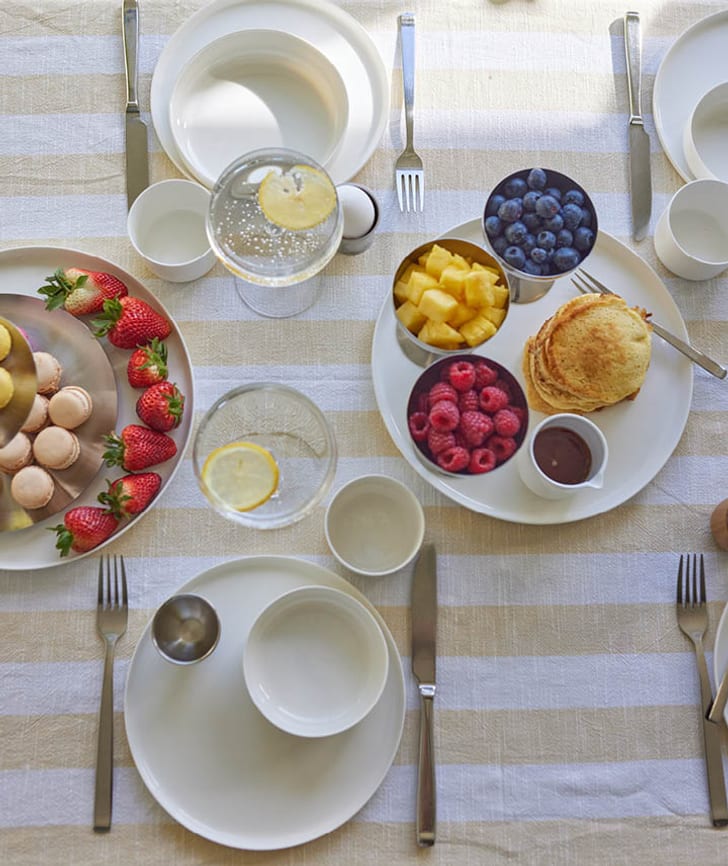 Ein gedeckter Tisch mit Pancakes, frischen Früchten, Macarons und Getränken.